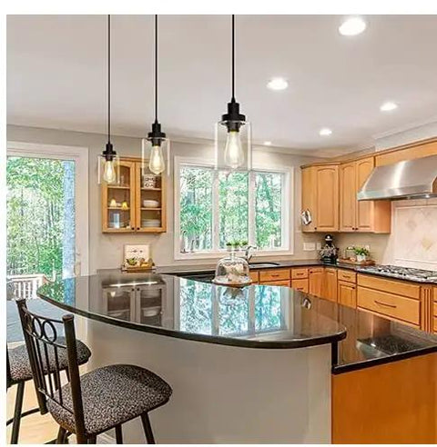 Three Pack Black Industrial Pendant Lights With Clear Glass Shades above a kitchen island with dark countertop and wooden cabinets.