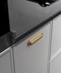 Close-up of installed Six Pack 5 Inch Antique Brass Cup Pulls With Distinctive Layered Ribbed Multi Sectioned Design on kitchen drawer.
