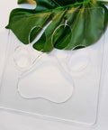 No Sweat Paw Print Router Template Crafted From Durable Clear Acrylic atop a green leaf, perfect for wood inlays and custom signs.