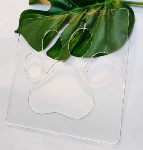 No Sweat Paw Print Router Template Crafted From Durable Clear Acrylic atop a green leaf, perfect for wood inlays and custom signs.