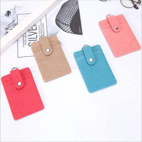 Four colored fabric card holders with snap button closure on a white surface.