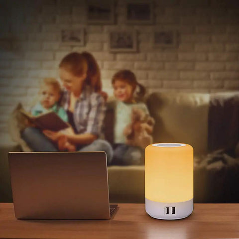 Touch Night Light Table Lamp With 4 USB Ports, Dimmable Warm White And 13 RGB Colors on a desk near a family on a sofa.