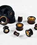 Two Tone Hollow Gold Stainless Steel And Sandalwood Ear Tunnels Plugs Set For Stretched Ears 0G To 1 Inch Double Flared Expander Hypoallergenic Body Jewelry 2 Pack Dope, showing various sizes on a display.
