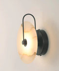 Nordic Style Stone Wall Lamp With Alabaster Finish, Metal Base Indoor Sconce For Living Room Dining Room Hallway Or Study, Cozy Glow Ambient Marble Look Wall Light For Modern Home Decor. Side view of lit alabaster wall sconce with black metal base.
