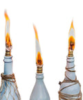 Three lit wine bottle torch kit with long life fiberglass wicks, brass wick holders, and brass caps for outdoor garden lighting.