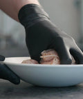 Close-up of black nitrile disposable gloves handling raw chicken in a white bowl