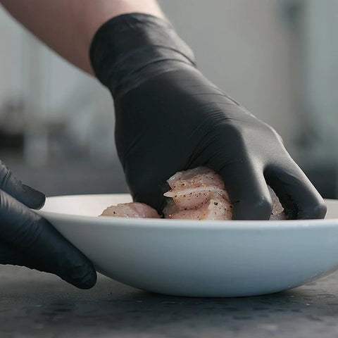 Close-up of black nitrile disposable gloves handling raw chicken in a white bowl