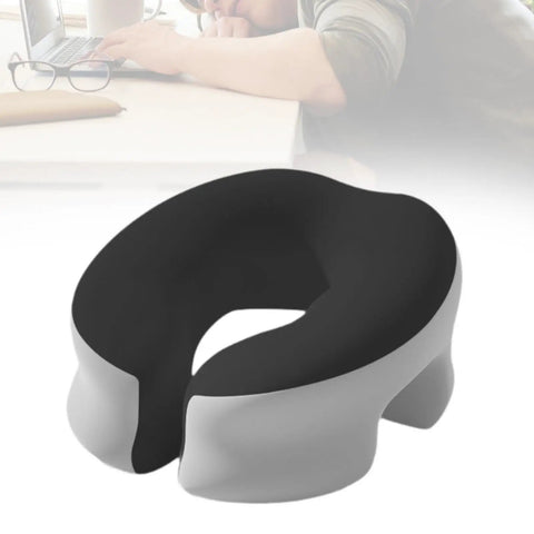 Black and light gray memory foam desk napping pillow with removable cover, shown on a desk next to a napping person.