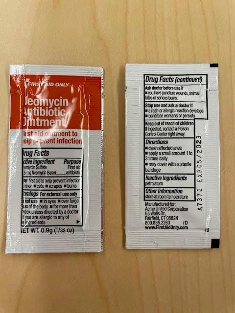 Front view of two red-and-white antibiotic ointment sachets with drug facts on a wooden surface.