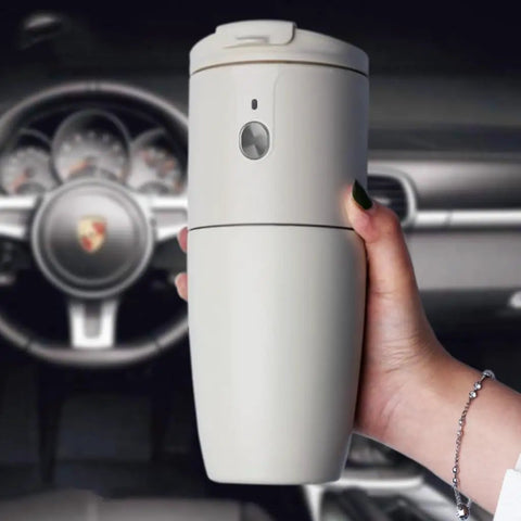 Compact Portable Coffee Maker With Built In Automatic Bean Grinder For Home Desk Or Road Trip, held in hand inside a car.