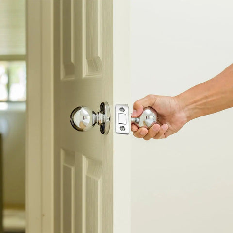 Person opening door with chrome doorknob, showcasing potential use for 20 Pack Ultra Thin Magnetic Cabinet Door Catches With Double Sided Tape And Screws.