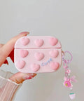 Hand holding pink heart-decorated case with cute word and strawberry charm, displaying decorative accessory for personalization.