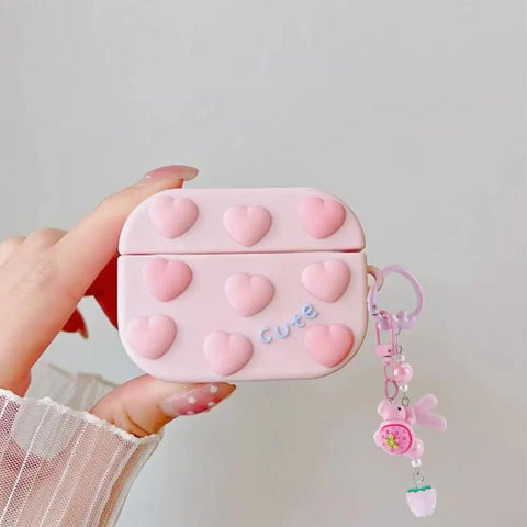 Hand holding pink heart-decorated case with cute word and strawberry charm, displaying decorative accessory for personalization.