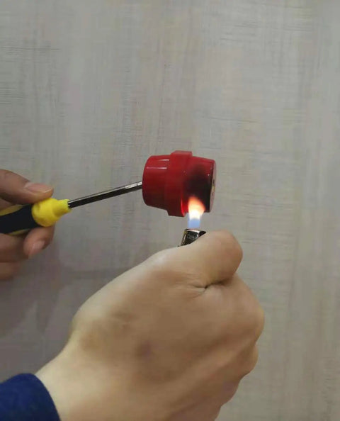Hand holding a red plastic cap and lighter, heating screwdriver tip