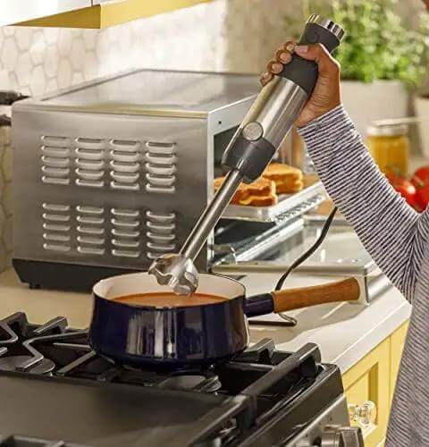 No Sweat 500 Watt Stainless Steel Immersion Blender With Removable Whisk And Spout Blending Jar For Thick Smoothies Quick Purees And Bold Homemade Sauces Dual Speed Hand Blender Kit in use blending sauce in a pot.
