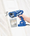 Professional Corded Airless Paint Sprayer With Triax Triple Piston Pump And Smart Control Dial held for easy use on a wall.