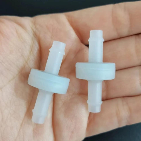 Close-up of two white PVDF 1/4 in barbed one-way check valves held in hand for spa ozone system