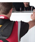 Shoulder Dolly 3500 heavy-duty lifting system in use by two people to lift a white appliance; black padded straps visible