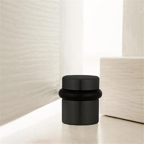 2 Pack Cylindrical Door Stops With Brass Construction And Oil Rubbed Bronze Finish floor mounted next to a door corner