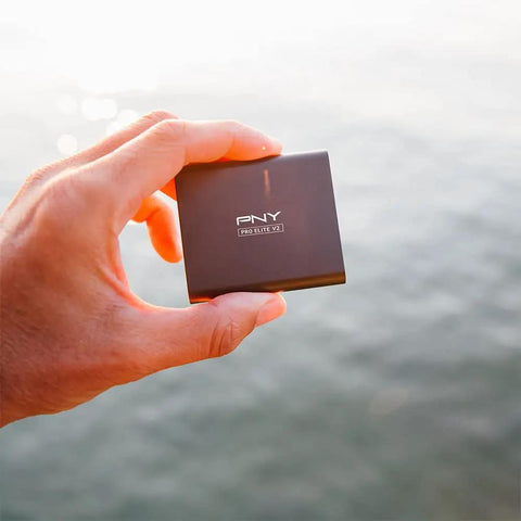 Person holding Pro Elite V2 1TB USB 3.2 Gen 2x1 Type-C External SSD For Gamers And Creators, Ultra Fast 1100 MB Per Second Read, 1000 MB Per Second Write against water backdrop