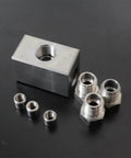 Angled view of a machined aluminum block with a central 1/4" threaded bore and four black bushings plus four silver threaded adapters.