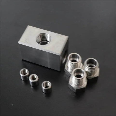 Angled view of a machined aluminum block with a central 1/4" threaded bore and four black bushings plus four silver threaded adapters.