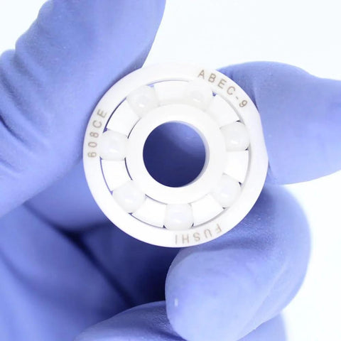Front view of a white 608 zirconia full-ceramic bearing held by gloved hand, showing outer race and ceramic balls.