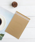 Bubble Mailers 16x22 CM Kraft Paper Self-Sealing Envelopes, 25 Pack on white surface next to coffee cup and pinecone.