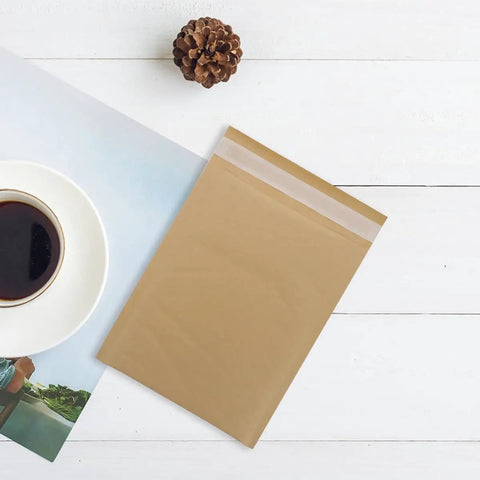 Bubble Mailers 16x22 CM Kraft Paper Self-Sealing Envelopes, 25 Pack on white surface next to coffee cup and pinecone.