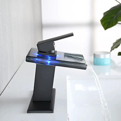 LED Temperature Sensing Slick Matte Black Bathroom Sink Faucet With Open Glass Spout Waterfall Flow Single Hole Mount Includes Metal Pop Up Drain And Two Water Supply Lines Color Changing Lights From Blue To Green To Red For Cold To Hot Water showing blue light