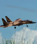 F-15 Twin 40mm EDF RC Fighter Jet PNP Desert Camo soaring above grass in flight with landing gear deployed, clear blue sky background.