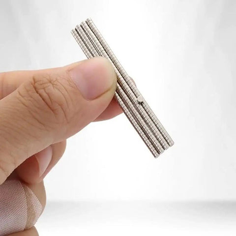 Hand holding stack of tiny Neodymium disc magnets, 2mm diameter by 1mm thick, nickel coated rare earth magnets, pack of 100