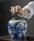A hand removing the lid from a solid ceramic tea canister for loose leaf storage, retro minimalist design.