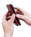 Hands holding a red and black smartphone together using the Universal Dual Phone Carrier With Strong Magnetic Mounts For Smart Device Storage.