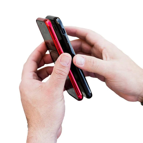 Hands holding a red and black smartphone together using the Universal Dual Phone Carrier With Strong Magnetic Mounts For Smart Device Storage.