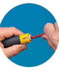 Hand using Lil Ripper Wire Stripper With Slitting Blade, V-Notch And Flat Blade Clip for NM cable stripping against blue background