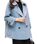 Light blue women's coat with wide collar and double-breasted buttons, worn over black dress with handbag.
