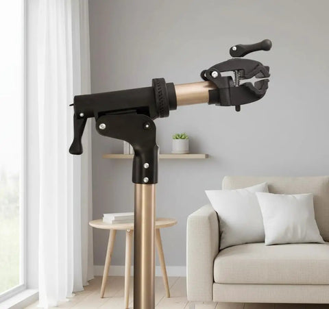 Foldable Aluminum Bike Repair Stand With Height Adjustable Arm in living room, showing clamp and metallic finish.