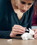 Front view: person applying Loctite Super Glue Liquid to a white ceramic rabbit figurine.