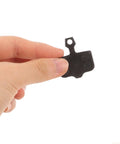 Hand holding a black, lightweight semi-metallic disc brake pad from Mountain Bike Disc Brake Pads, 4 Pairs, Lightweight Semi Metallic Replacement Kit For Hydraulic Systems, Wear Resistant Pads Deliver Quiet, Trail Ready Stopping Power On Trails And Mountain Rides.