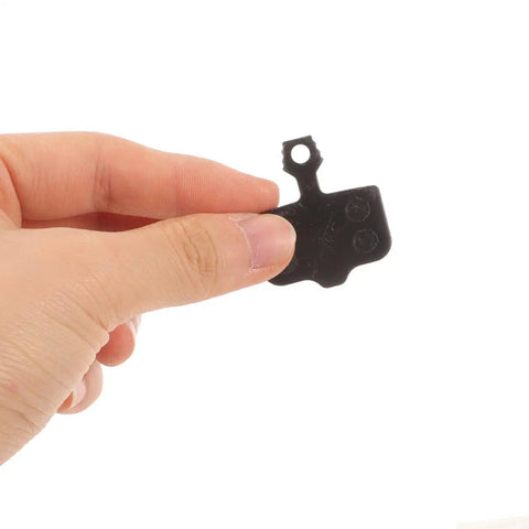 Hand holding a black, lightweight semi-metallic disc brake pad from Mountain Bike Disc Brake Pads, 4 Pairs, Lightweight Semi Metallic Replacement Kit For Hydraulic Systems, Wear Resistant Pads Deliver Quiet, Trail Ready Stopping Power On Trails And Mountain Rides.