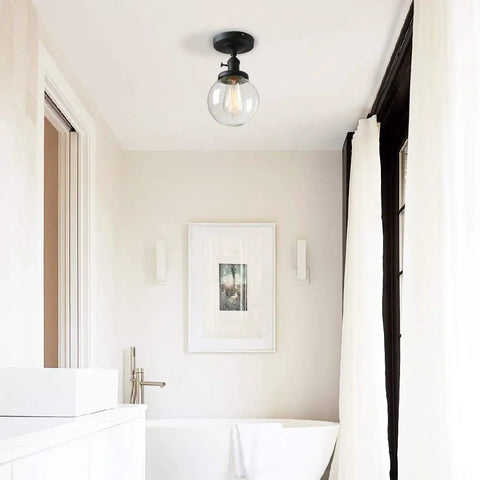 Slick Modern Semi Flush Mount Ceiling Light With Handblown Clear Glass Globe Shade in a bathroom, black finish, E26 LED compatible.