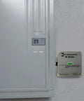 Advanced Outdoor Surge Protector With TPMOV Technology mounted on gray wall beside electrical panel, beefed up green status LED