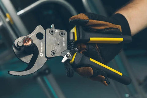 Gloved hand holding Ratcheting Cable Cutter With Two Step Mechanism For Clean Copper And Aluminum Cuts Up To 600 MCM