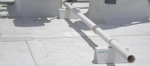 Front view of 4-pack white PVC rooftop pipe support blocks on a flat white roof with Rooftop logo