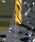 Titanium-coated drill bit drilling into metal plate; gold-colored, close-up view