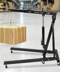 Badass Two Ton Folding Hydraulic Engine Lift Crane lifting a package, featuring heavy duty carbon steel and swivel wheels.