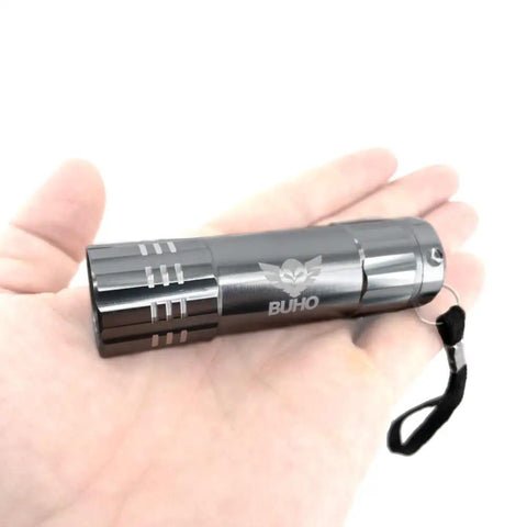 Hand holding compact silver flashlight with lanyard, part of Ryobi 18V Cordless Hybrid Portable Fan Bundle With Seven And A Half Inch Blade 2.0 Ah Battery 18 Volt Charger And Flashlight Three Speed Settings 160 Degree Pivot Head Built In Handle And Hanging Options Works With Extension Cords.