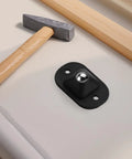 Close-up of a black self-adhesive swivel caster wheel mounted, with a hammer and wood piece, for 12 Pack Self Adhesive Swivel Caster Wheels With 360 Degree Spin Hassle Free Rolling Pads For Kitchen Cabinets And Moving Crates Tough Abs Sticky Roller Kit Quiet Black Low Profile Glide.