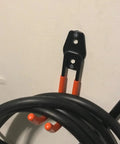 Keep Your EV Charging Cord Squared Away With This Rugged Wall Mount J Hook That Hangs Electric Vehicle Cables Up High To Dodge Rain And Dust For Stress Free Plugging Whenever You Need It; black and orange j hook mounted on wall with EV charging cord.